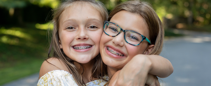 Trommeter Orthodontics | Two young girls outdoors smiling and hugging each other, both wearing braces.