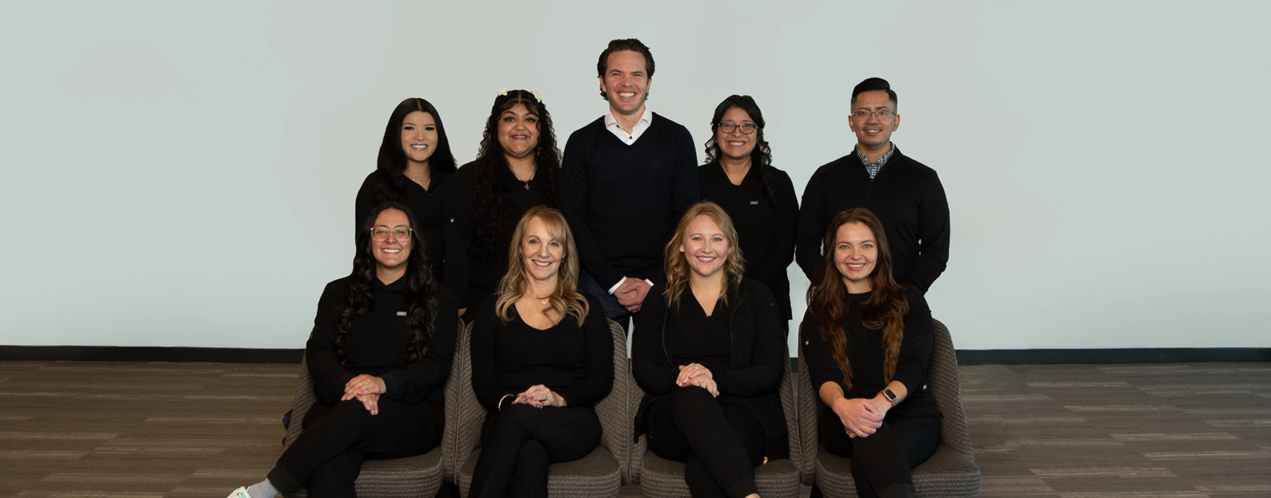 Trommeter Orthodontics | Group photo of Trommeter Orthodontics team members smiling, dressed in black attire.