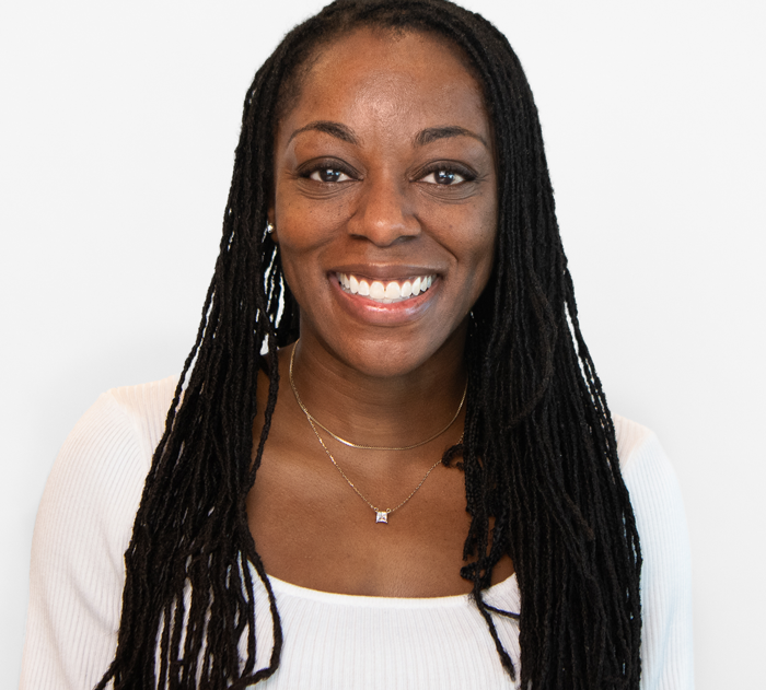 Trommeter Orthodontics | Portrait of a smiling woman with long black locs, wearing a white top and layered gold necklaces.