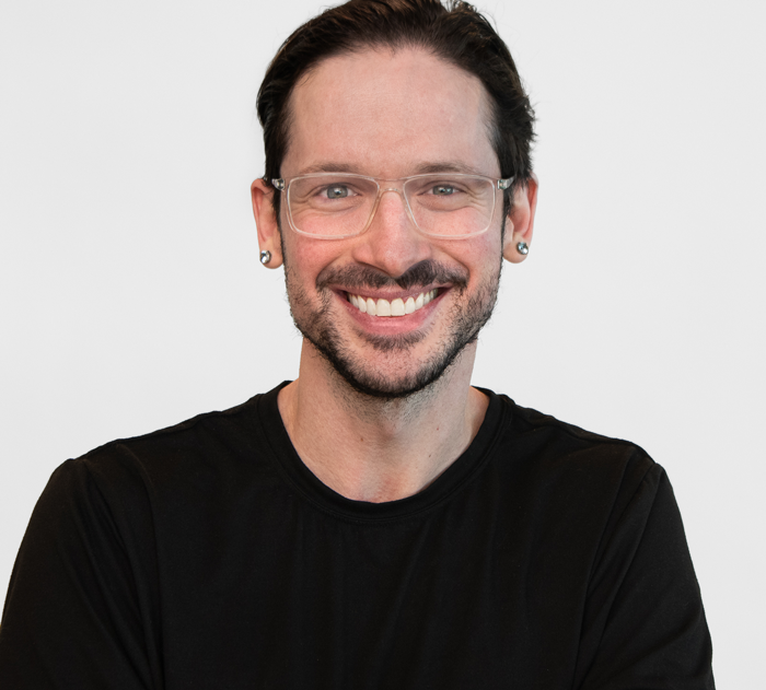 Trommeter Orthodontics | Portrait of a smiling man with short dark hair, glasses, and earrings, wearing a black shirt.