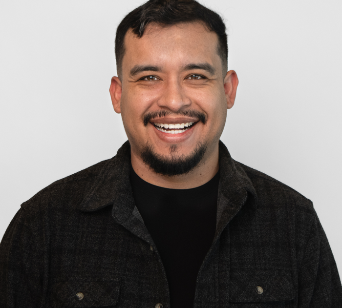 Trommeter Orthodontics | Portrait of a smiling man with short dark hair, mustache and goatee, wearing a black textured button-up shirt.
