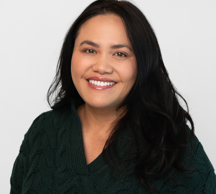Trommeter Orthodontics | Portrait of a smiling woman with long black wavy hair, wearing a dark green sweater.